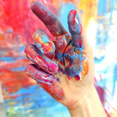 Dłoń ubrudzona farbą, w tle kolorowy obraz